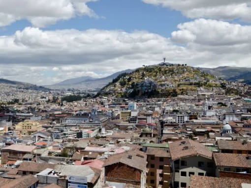 Vista de los tejados del Centro Histórico de Quito desde la Basílica del Voto Nacional, con el Panecillo difuminado en el fondo bajo un cielo parcialmente nublado.