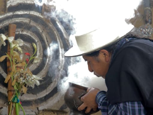 Plumas de humo se elevan de un cuenco de cerámica mientras un Saraguro sopla en él.